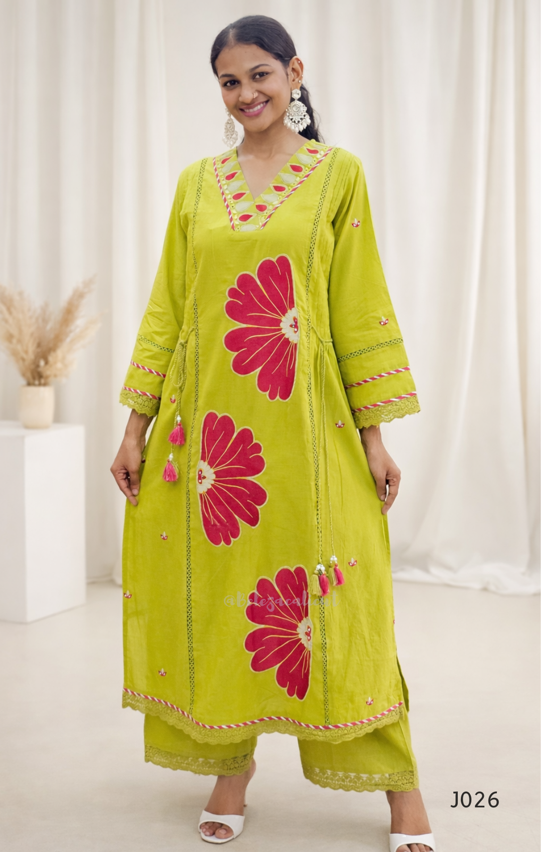 Woman wearing a green kurta with pink floral patterns in a minimal indoor setting.