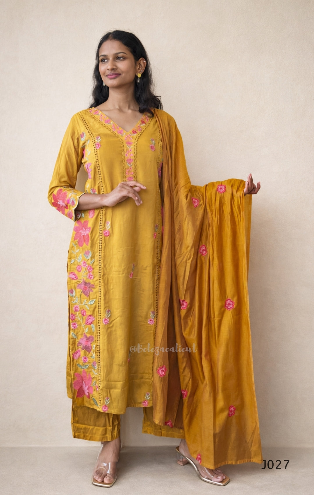 Woman wearing a yellow embroidered traditional outfit with a plain background