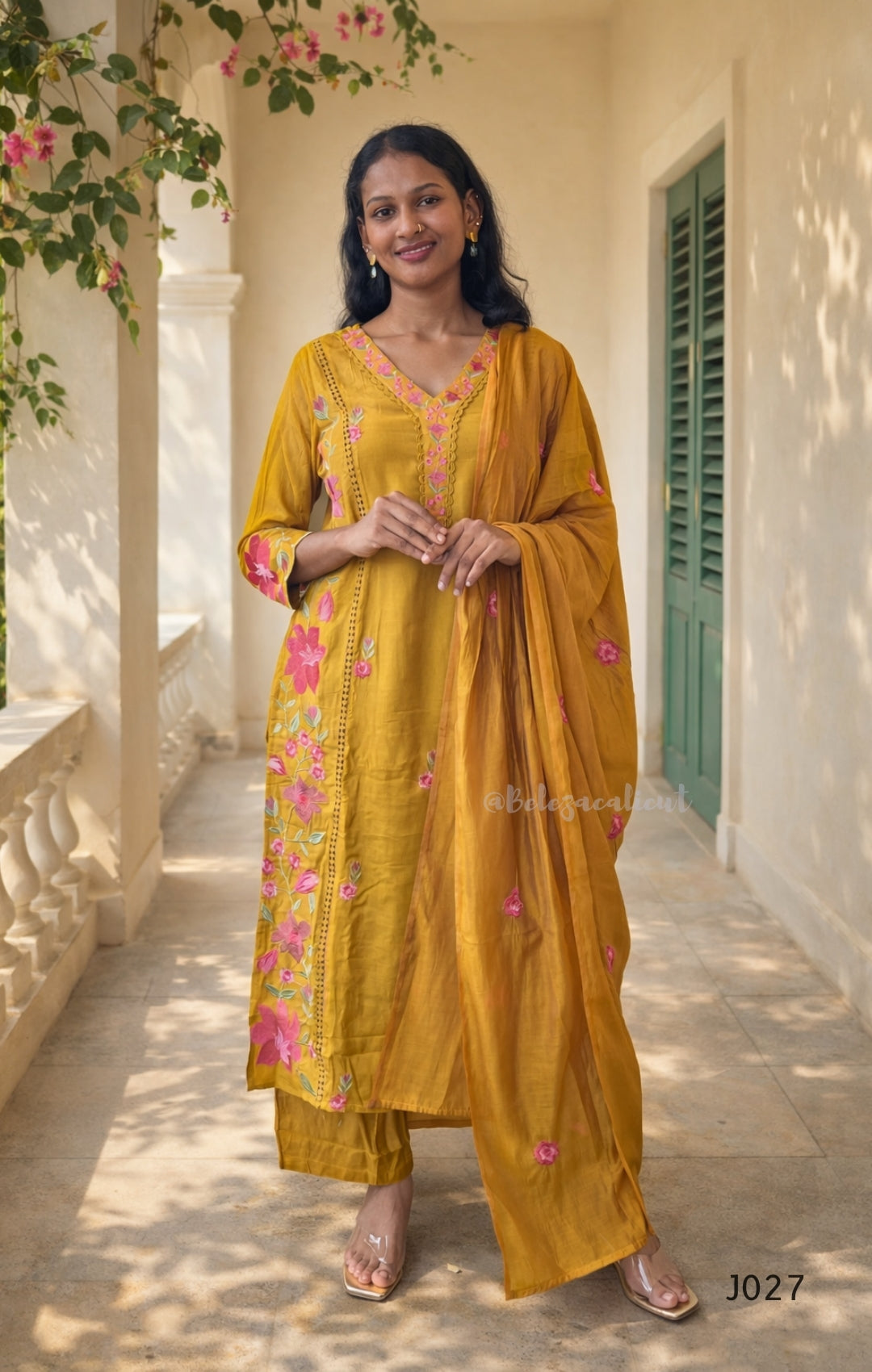 Woman wearing a mustard yellow traditional outfit with pink floral patterns on a balcony.