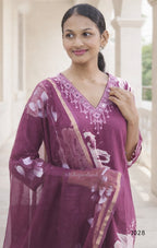 Woman wearing a purple traditional outfit with floral patterns in an outdoor setting.