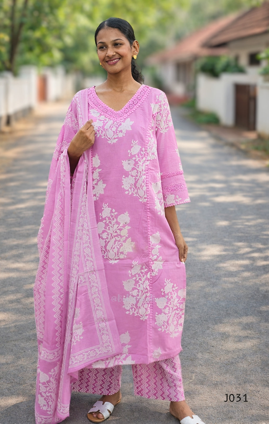 Woman wearing a pink traditional outfit with white floral patterns on a road.