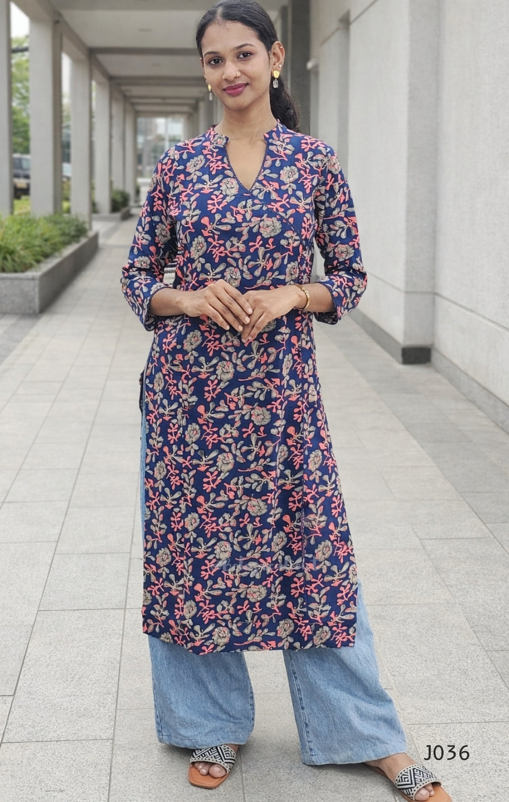 Woman wearing a floral kurta with blue pants standing on a sidewalk.