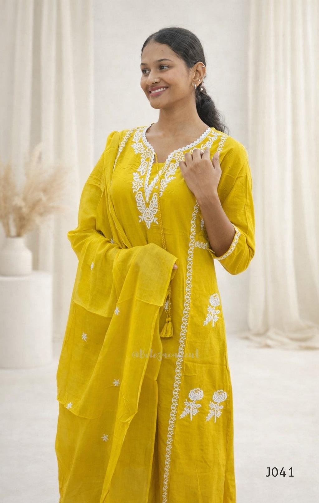Woman wearing a yellow traditional outfit with white embroidery in a neutral setting