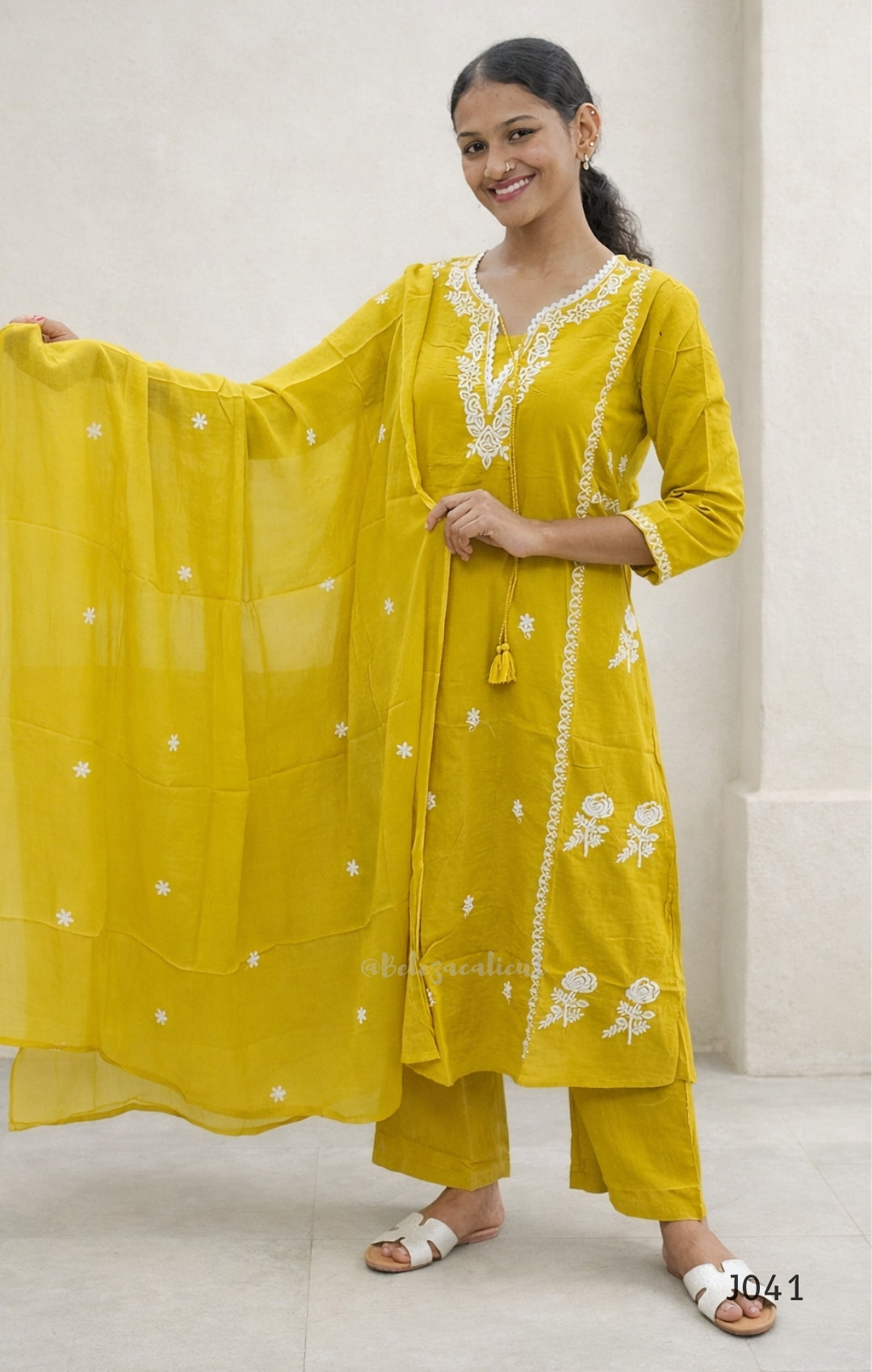 Woman wearing a yellow traditional outfit with white embroidery against a white background