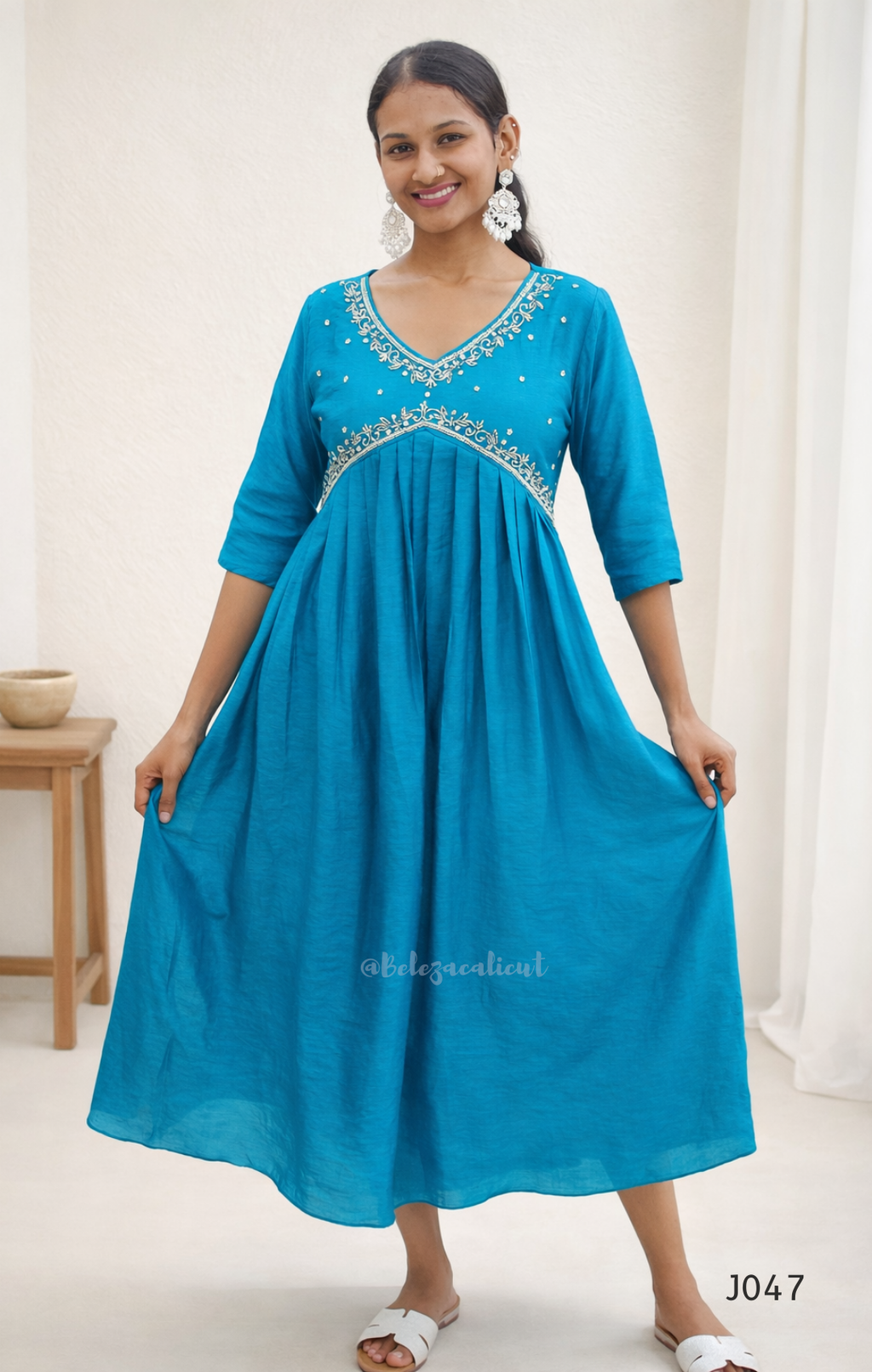 Woman wearing a blue dress with intricate detailing in a minimal indoor setting