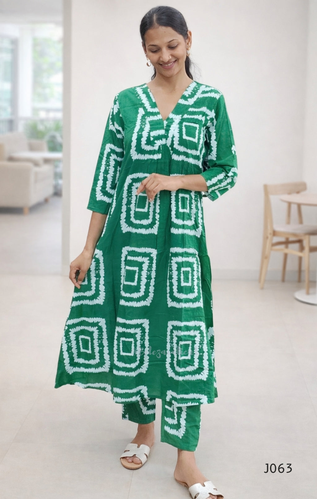 Woman wearing a green dress with white geometric patterns in a bright room.