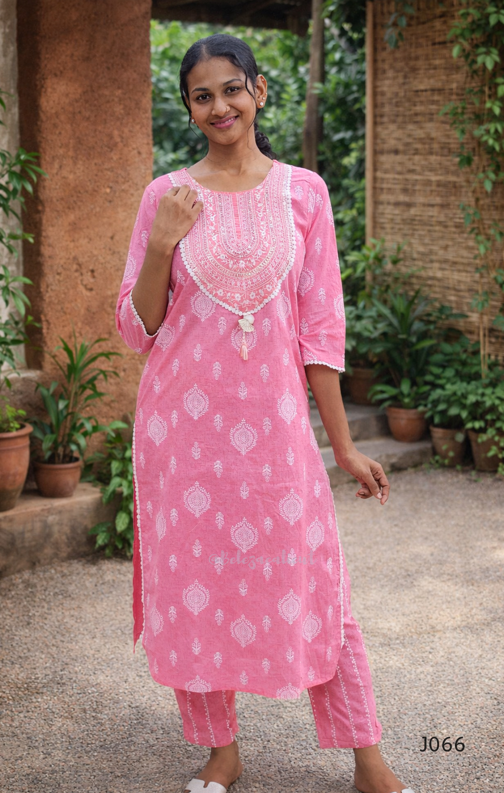 Woman wearing a pink traditional outfit with white patterns in an outdoor setting.