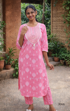 Woman wearing a pink traditional outfit with white patterns in an outdoor setting.