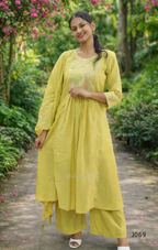 Woman in a yellow traditional outfit standing in a garden with greenery and flowers.
