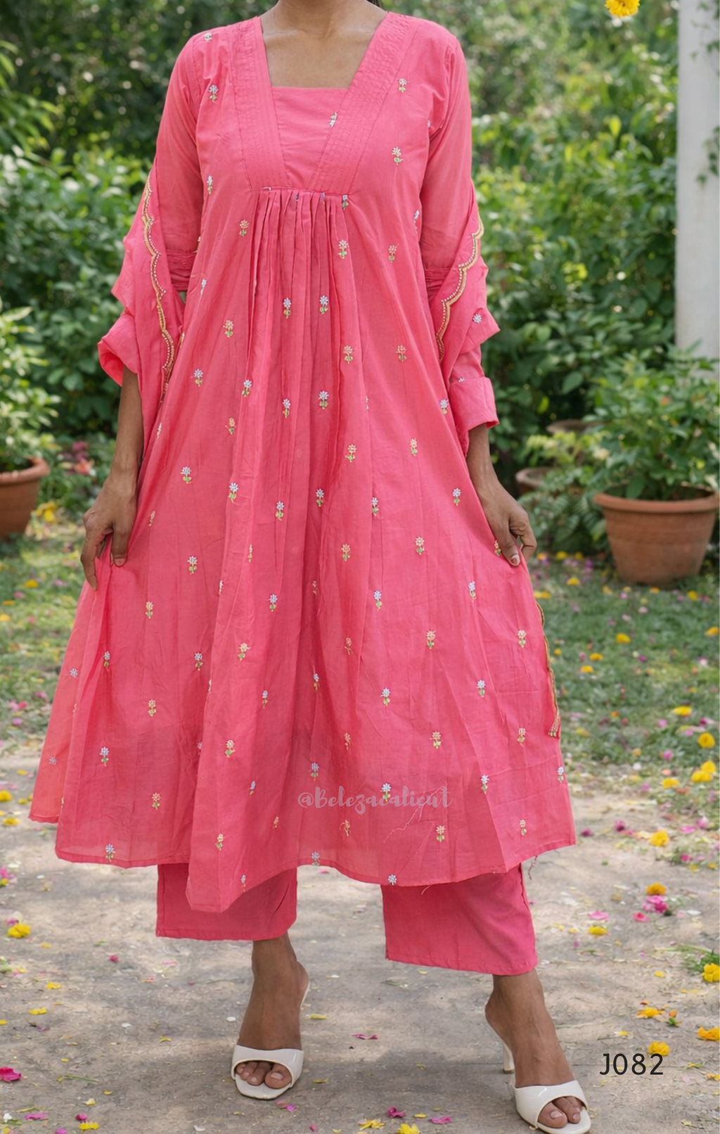 Woman wearing a pink traditional outfit with floral patterns in an outdoor setting.