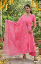 Woman in a pink traditional outfit with a matching dupatta, standing outdoors with greenery in the background.