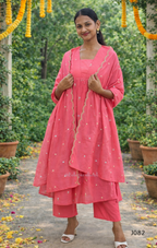 Woman in a pink traditional outfit standing outdoors with greenery and decorations.