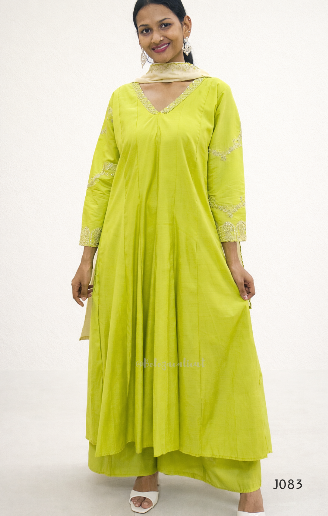 Woman wearing a bright green dress with white embroidery on a white background