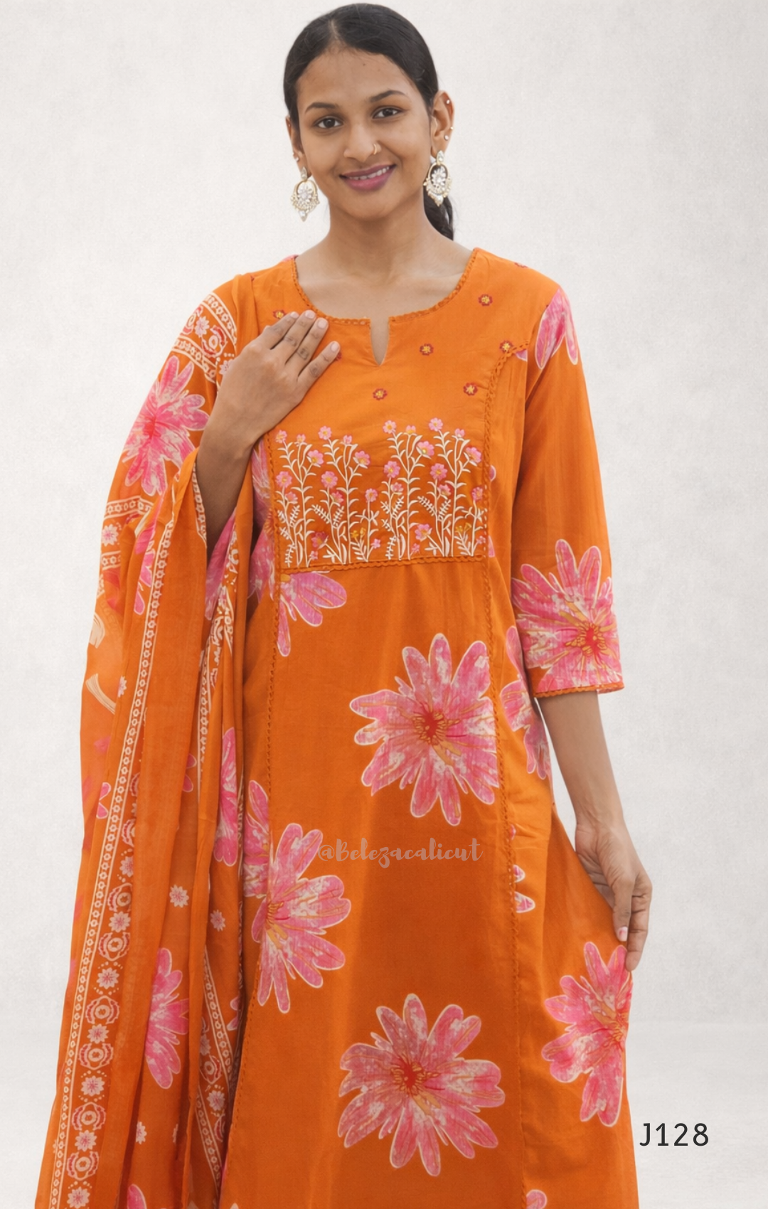 Woman wearing an orange kurta with pink floral patterns and a matching dupatta on a white background