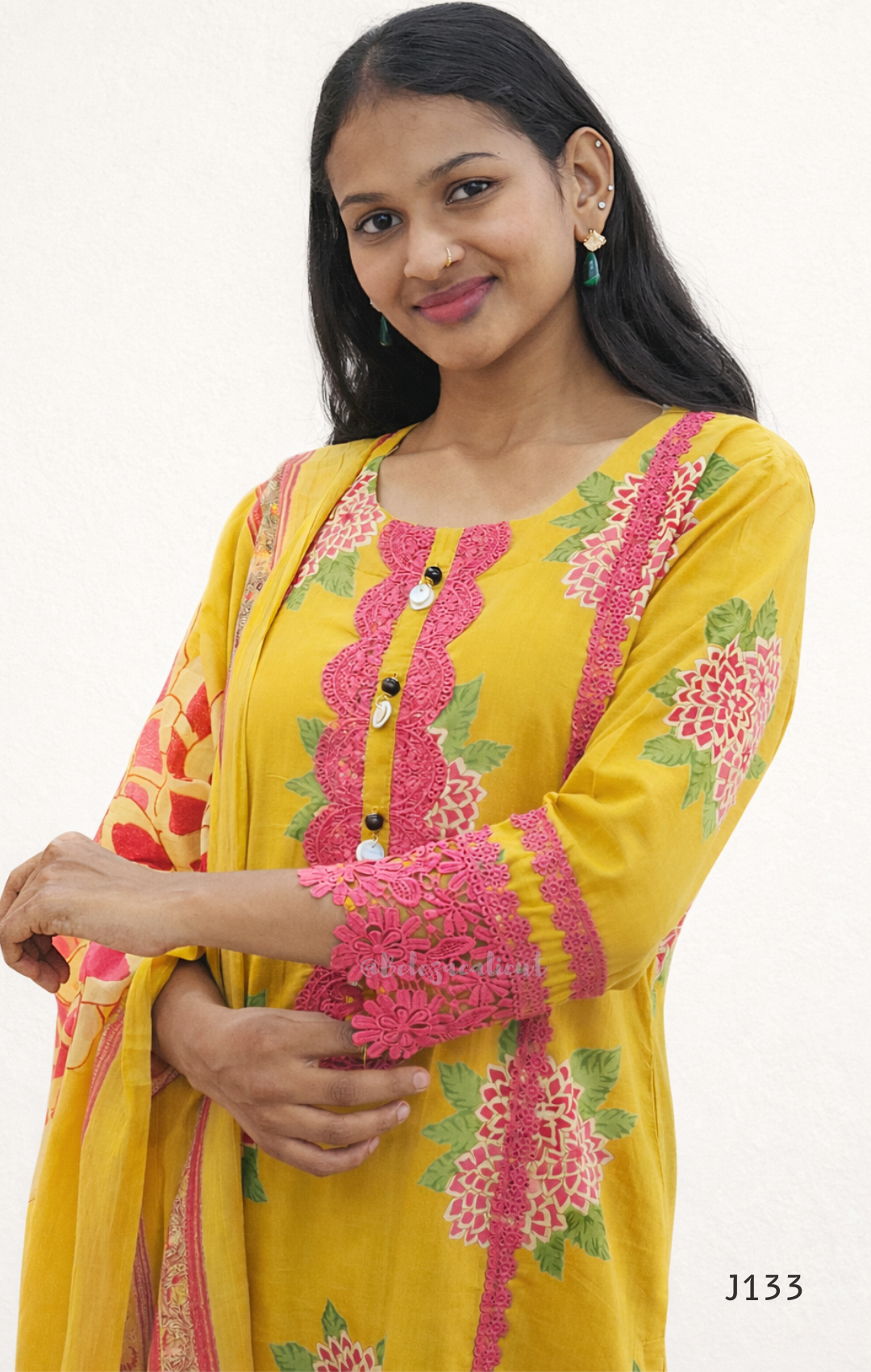 Woman wearing a yellow dress with pink and green embroidery on a white background