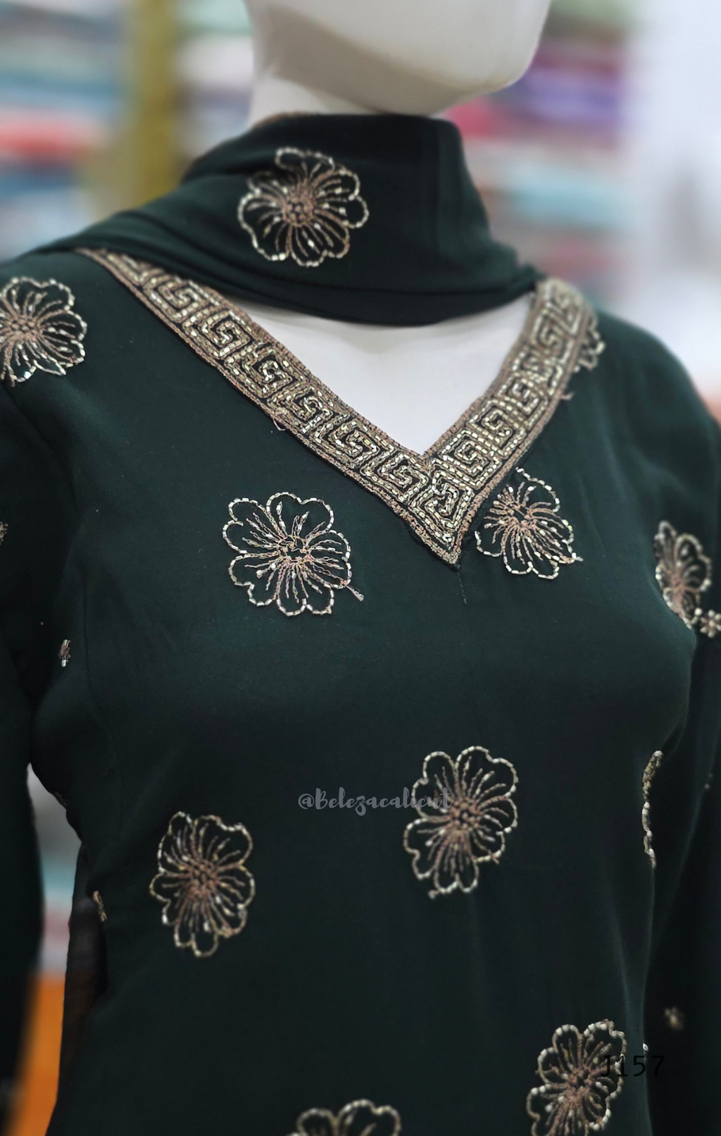 Dark green garment with floral embroidery on a mannequin against a blurred background