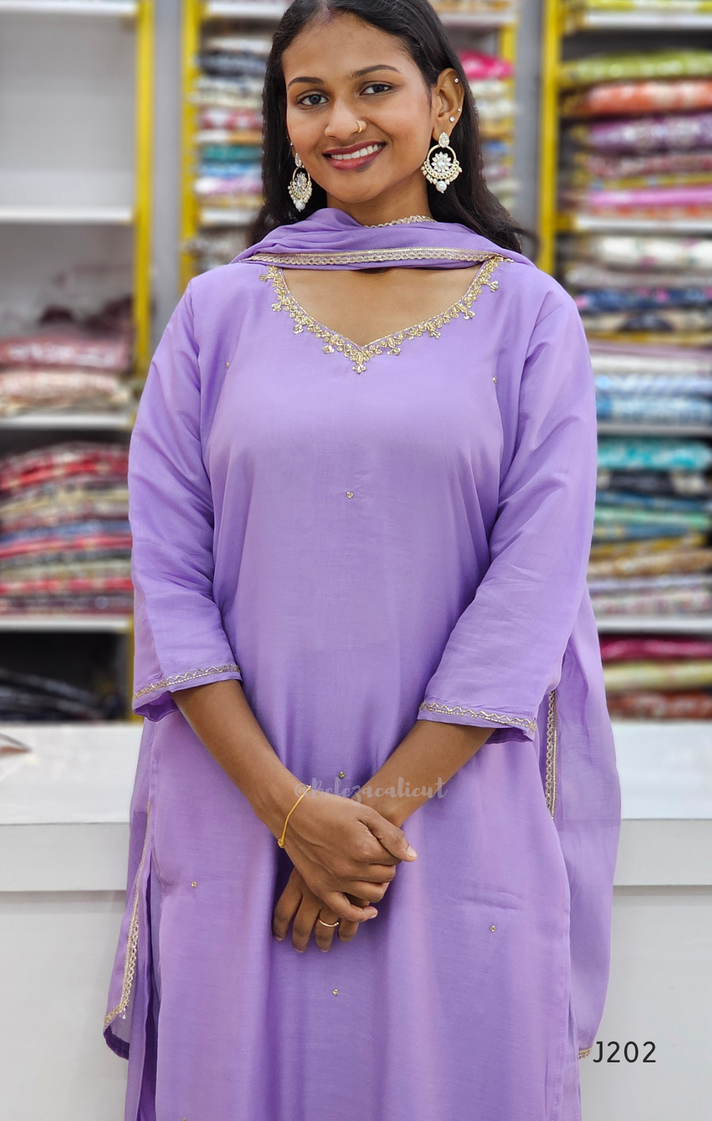 Woman wearing a light purple traditional outfit with gold embroidery in a fabric store.