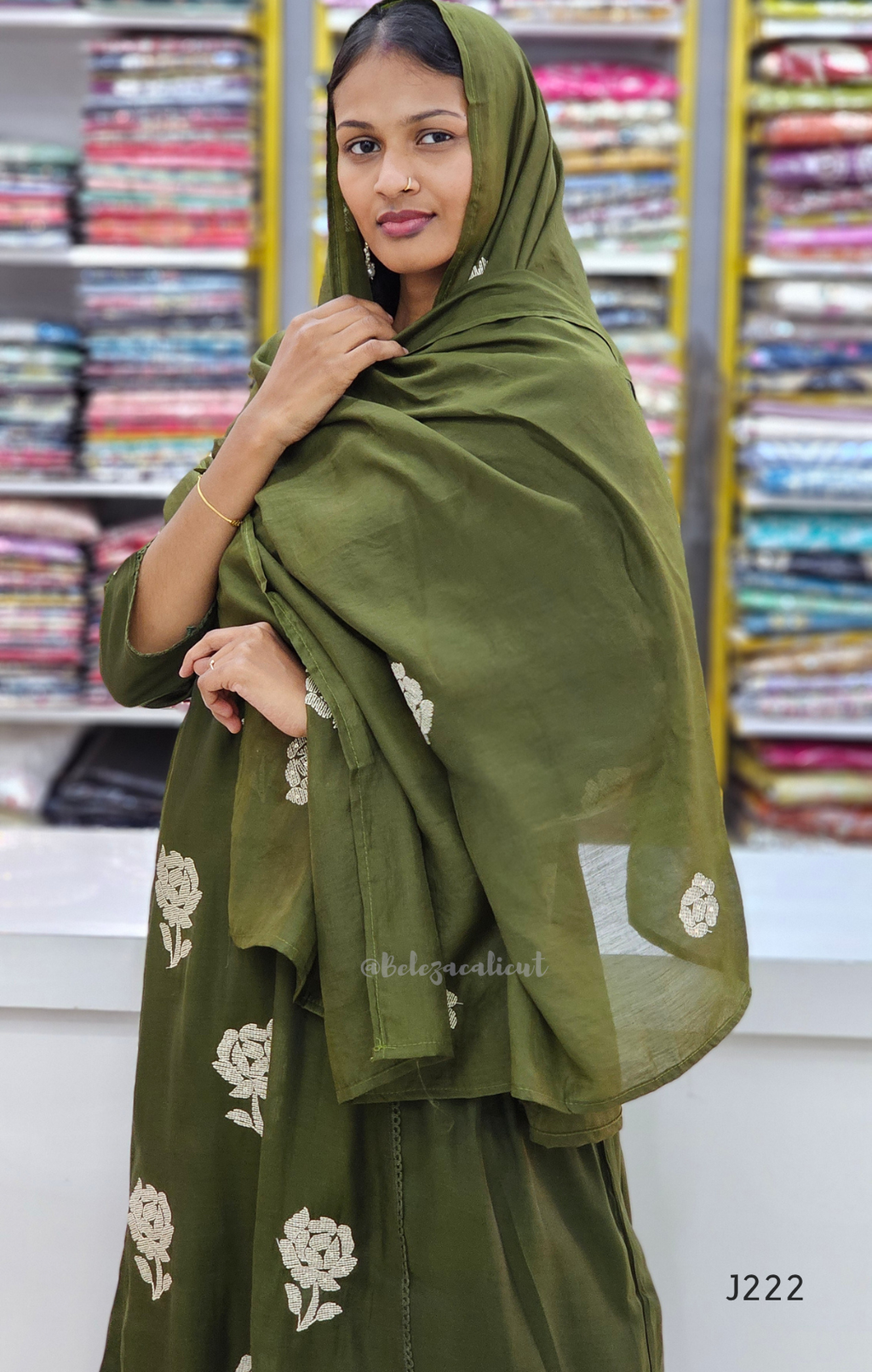 Woman wearing a green traditional outfit with floral patterns in a fabric store.
