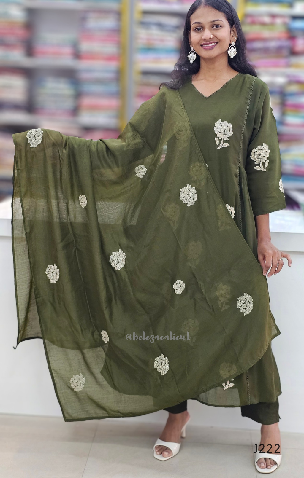 Woman wearing a green traditional outfit with floral patterns in a blurred indoor setting