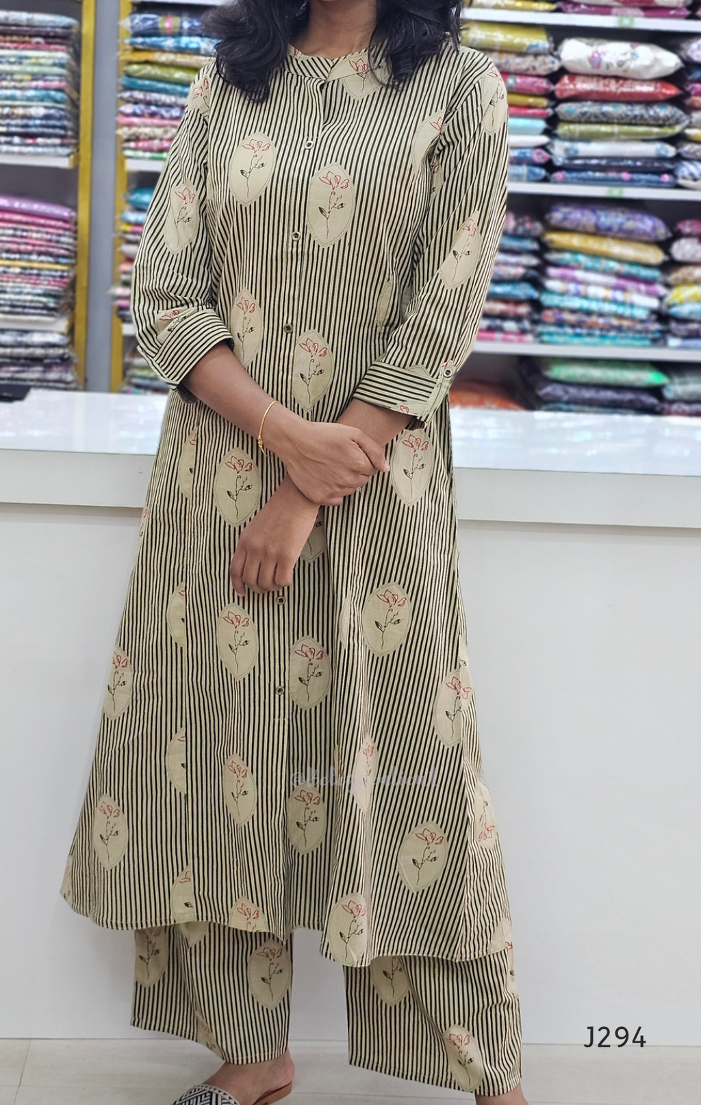 Person wearing a floral and striped outfit with a background of fabric rolls.