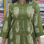 Green kurta with white floral patterns worn by a person, with a fabric store background.