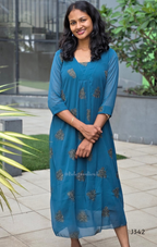 Woman wearing a blue dress with floral patterns standing outdoors.