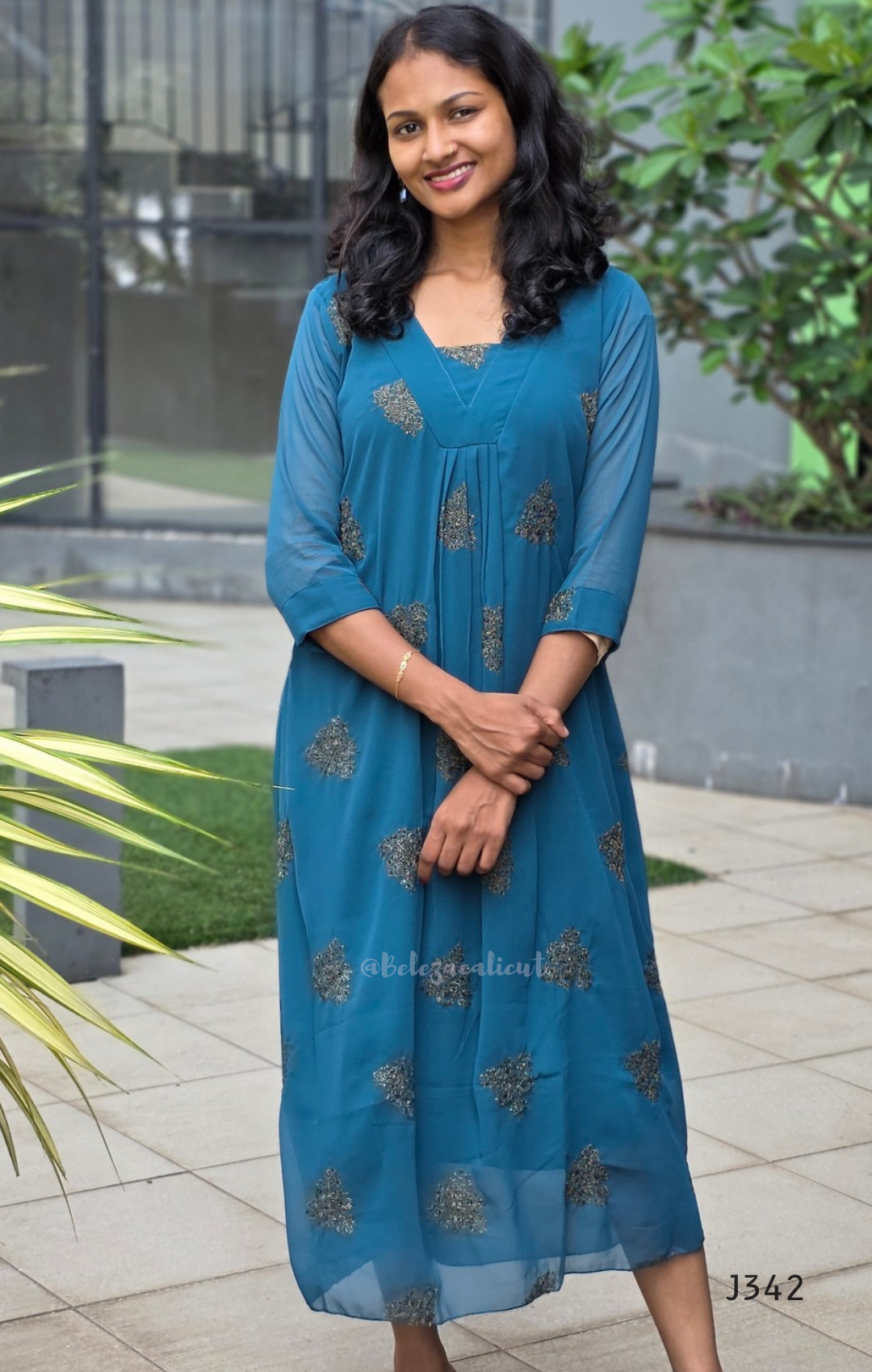 Woman wearing a blue dress with floral patterns standing outdoors.