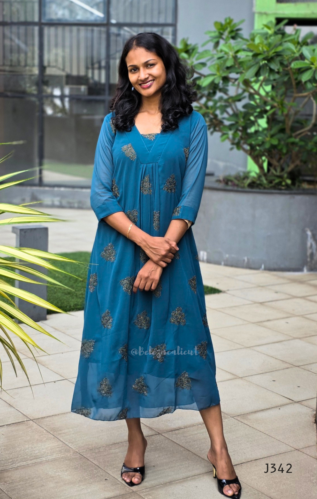 Woman wearing a blue dress with floral patterns standing outdoors.