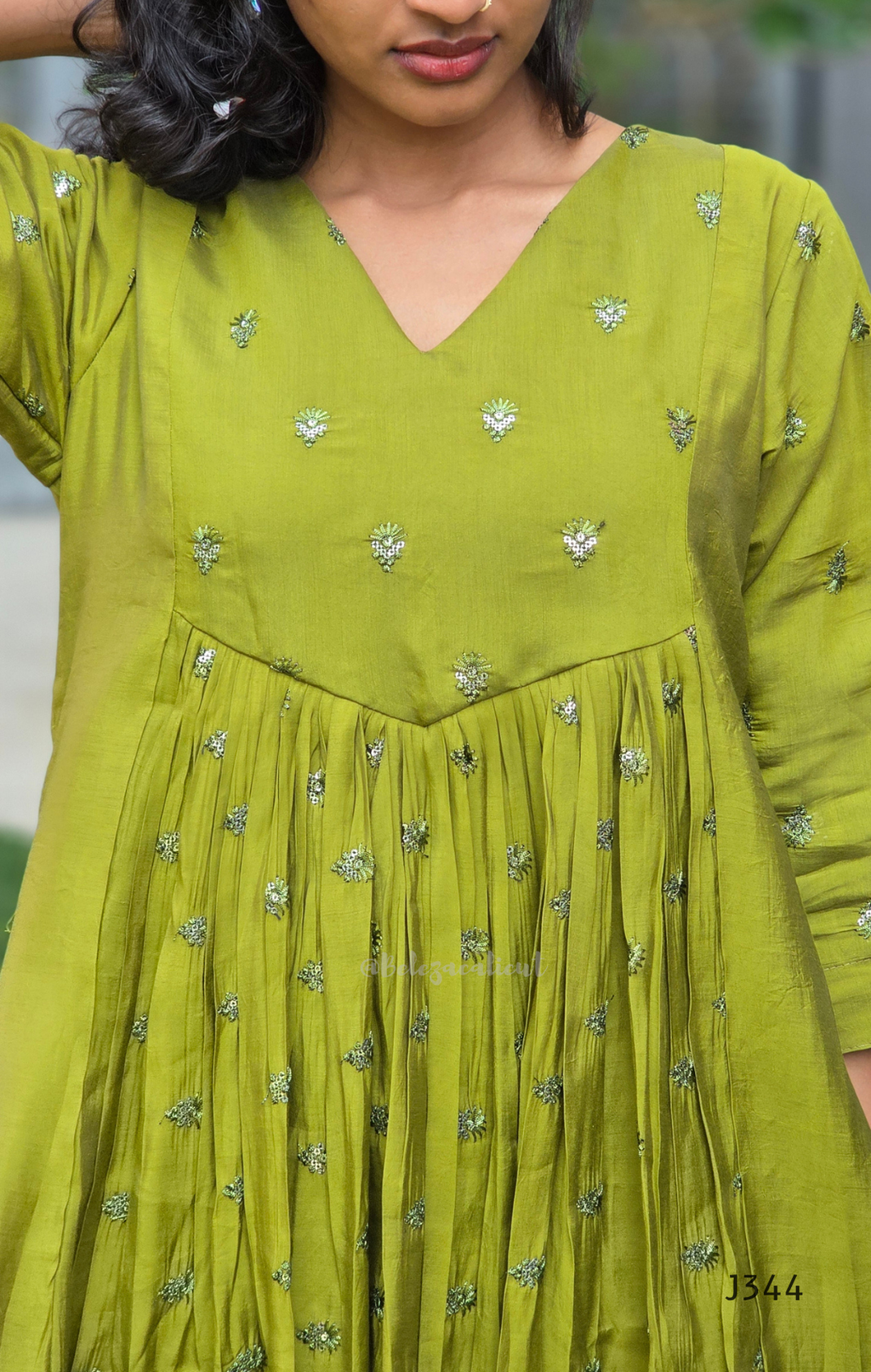Green dress with floral patterns worn by a person, blurred background