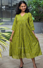 Woman wearing a green dress standing outdoors with plants in the background