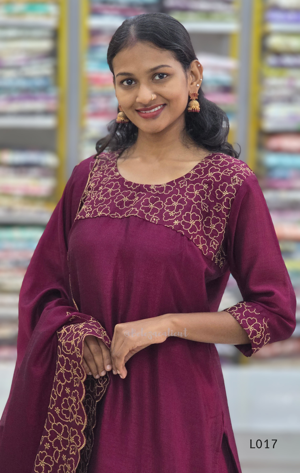Woman wearing a maroon traditional outfit with gold embroidery in a fabric store.