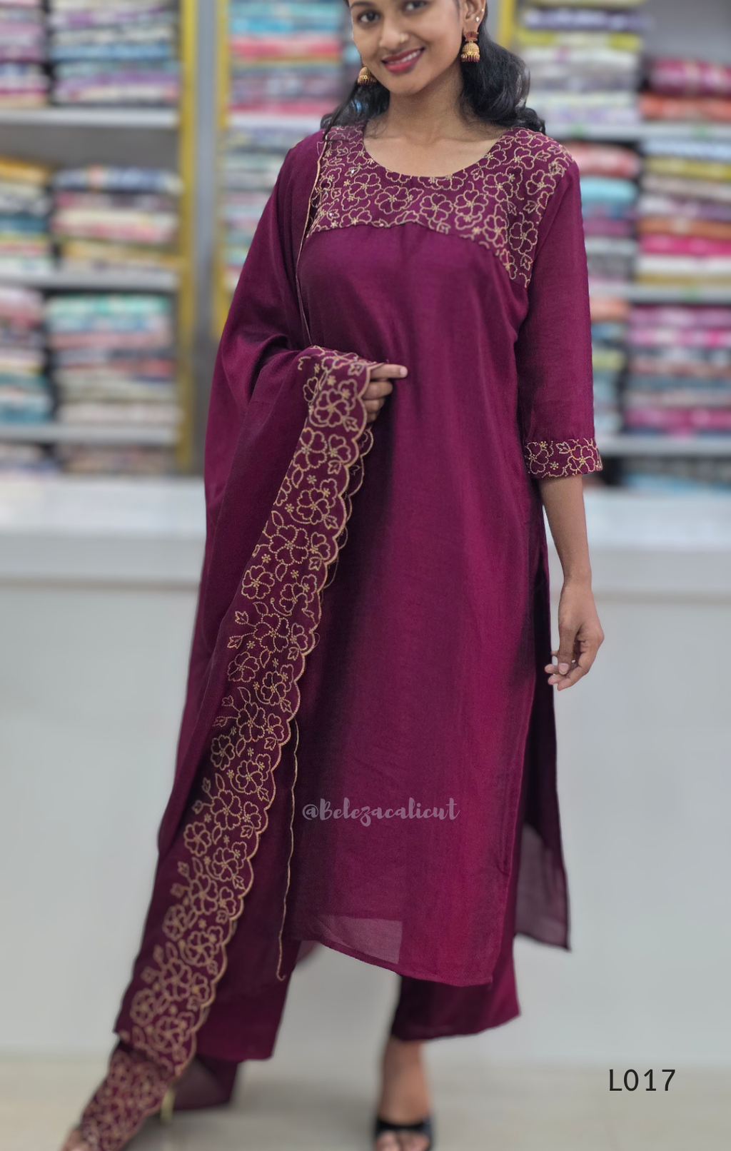 Woman wearing a maroon traditional outfit with intricate embroidery in a store setting.