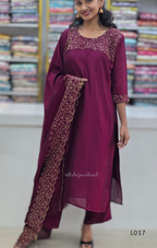 Woman wearing a maroon traditional outfit with intricate embroidery in a store setting.