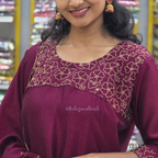 Woman wearing a maroon traditional outfit with gold embroidery, standing in a store.