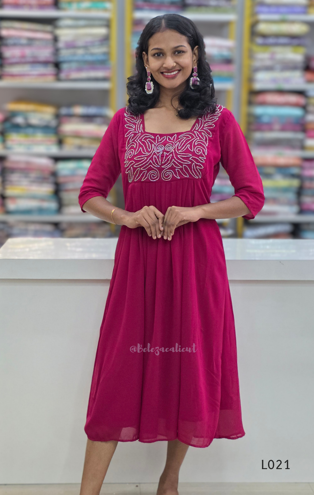 Woman wearing a pink dress with white embroidery in a bookstore setting