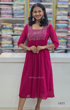 Woman wearing a pink dress with white embroidery in a bookstore setting