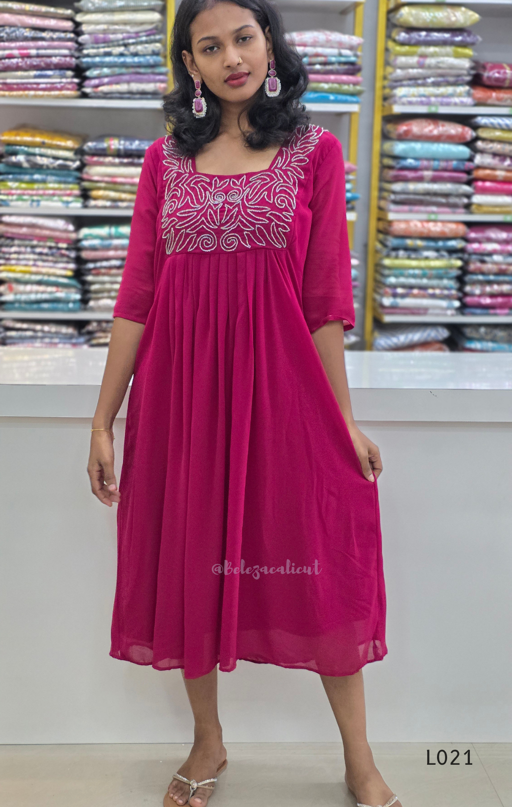Woman wearing a pink dress with white embroidery in a fabric store.