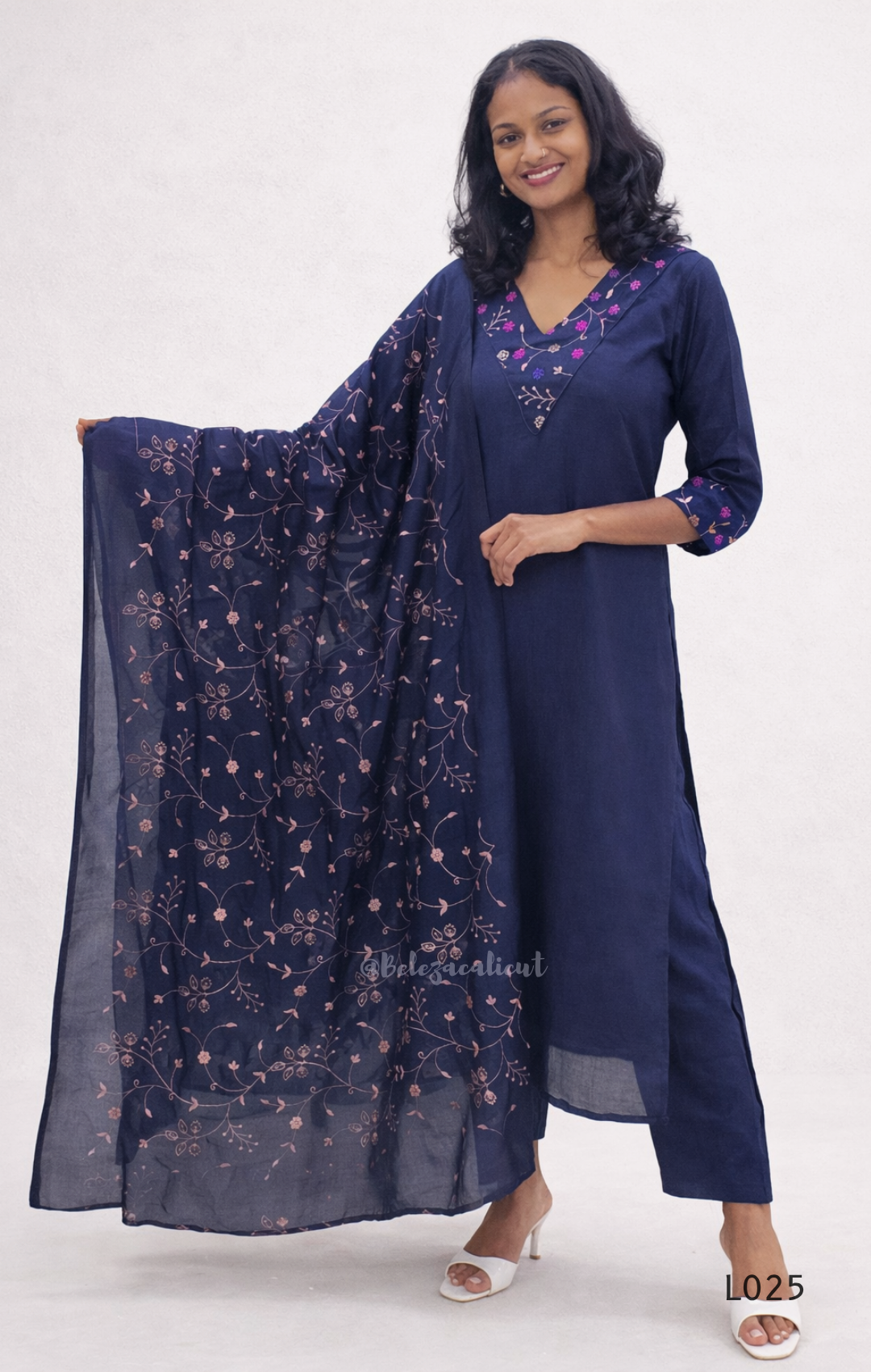 Woman wearing a navy blue dress with floral embroidery and a matching scarf on a white background