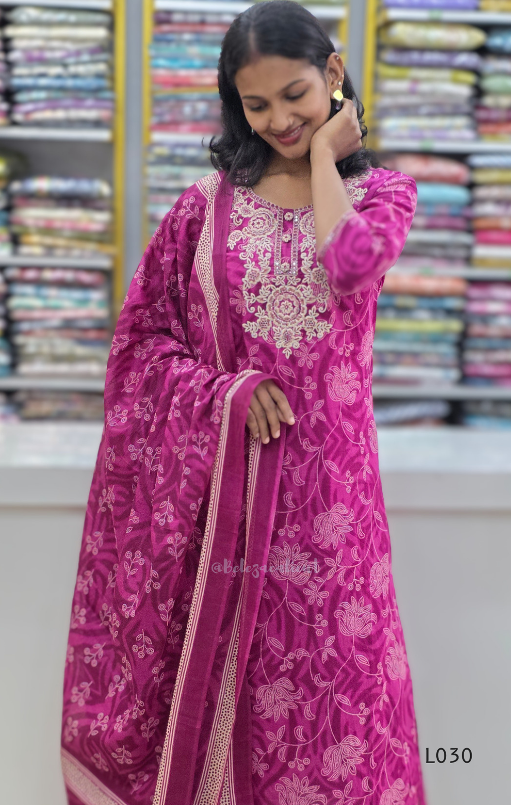 Woman wearing a pink embroidered traditional outfit with a colorful fabric background