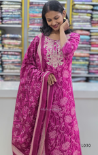 Woman wearing a pink embroidered traditional outfit with a colorful fabric background