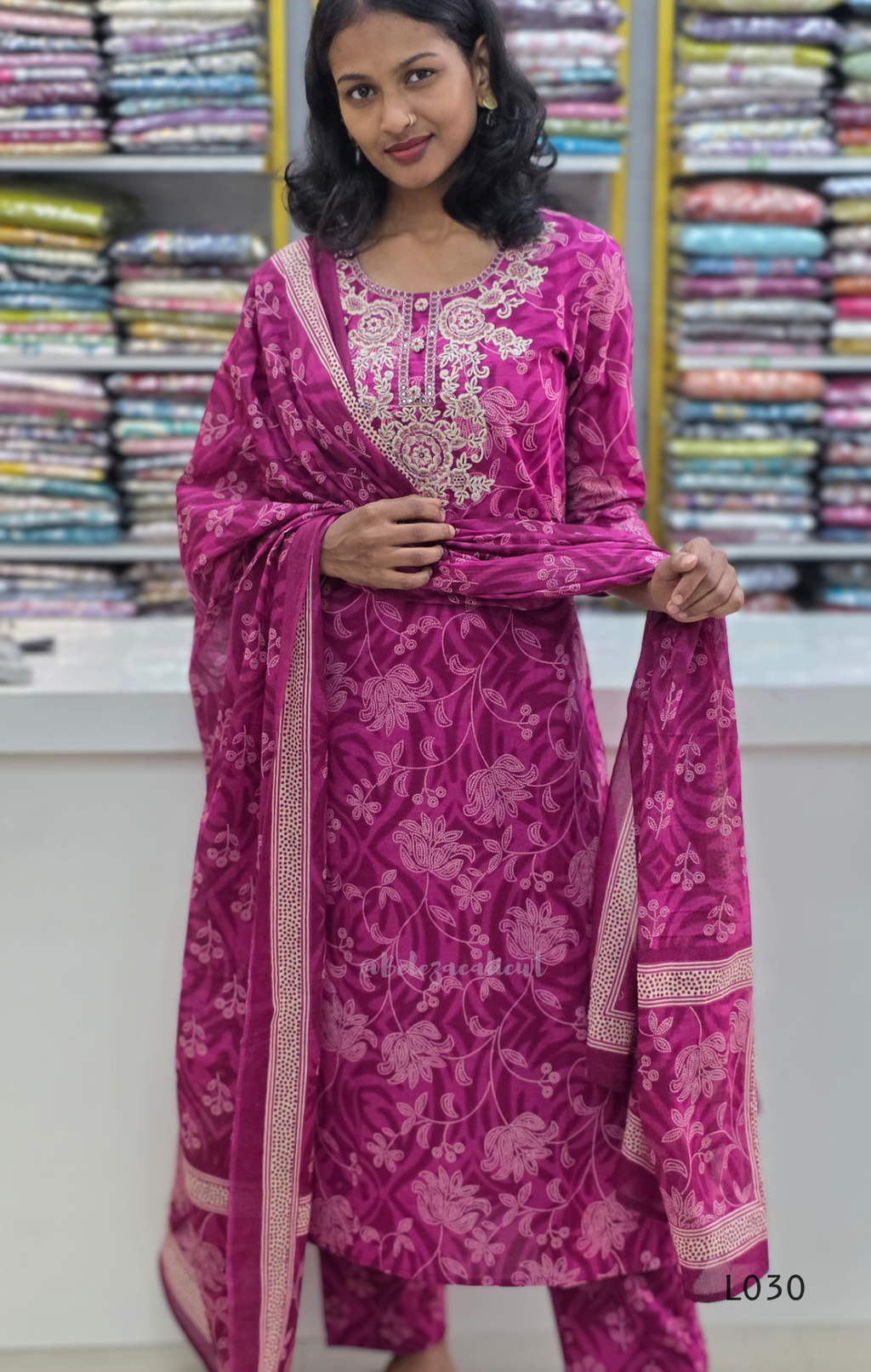 Woman wearing a pink traditional outfit with floral patterns in a store setting.