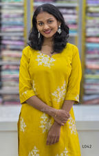 Woman wearing a yellow kurta with white floral embroidery in front of a fabric store.