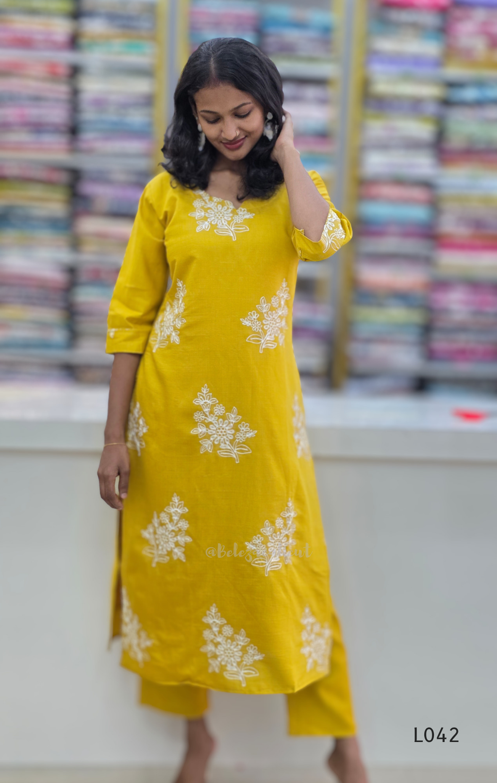 Woman wearing a yellow kurta with white floral patterns in a fabric store.