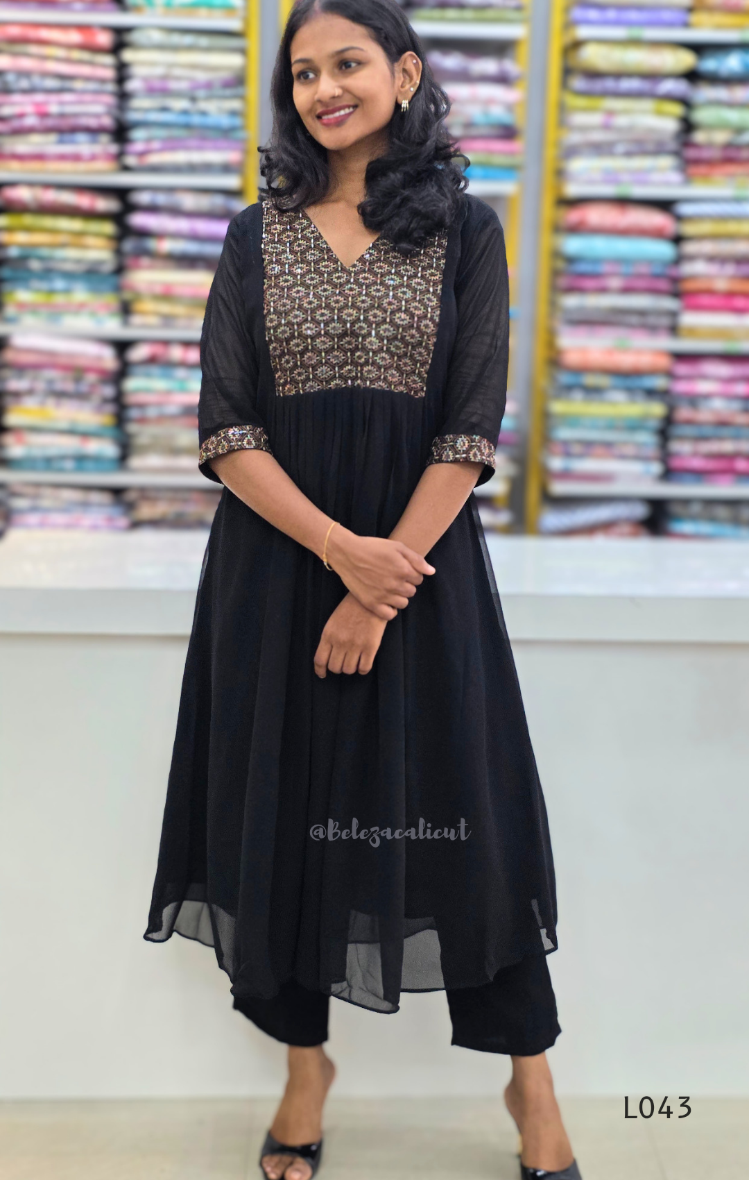 Woman wearing a black dress with patterned top in front of colorful fabric background