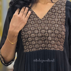 Black dress with gold geometric pattern worn by a person, with a blurred background.