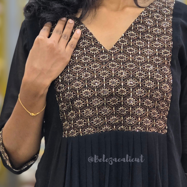 Black dress with gold geometric pattern worn by a person, with a blurred background.