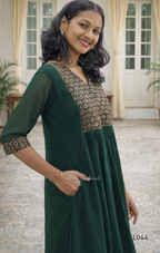Woman wearing a green traditional outfit with floral patterns indoors.