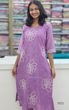 Woman wearing a purple dress with floral patterns in front of a colorful fabric background
