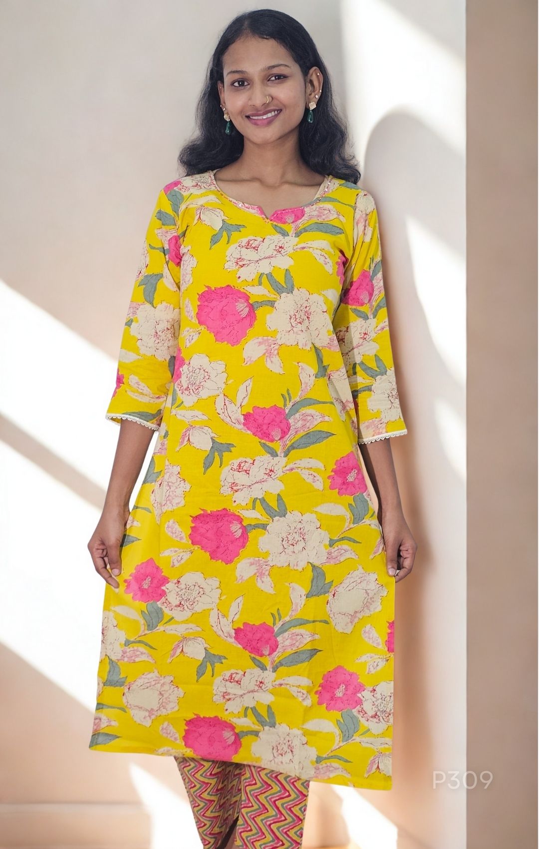 Woman wearing a yellow floral dress standing indoors with a neutral background
