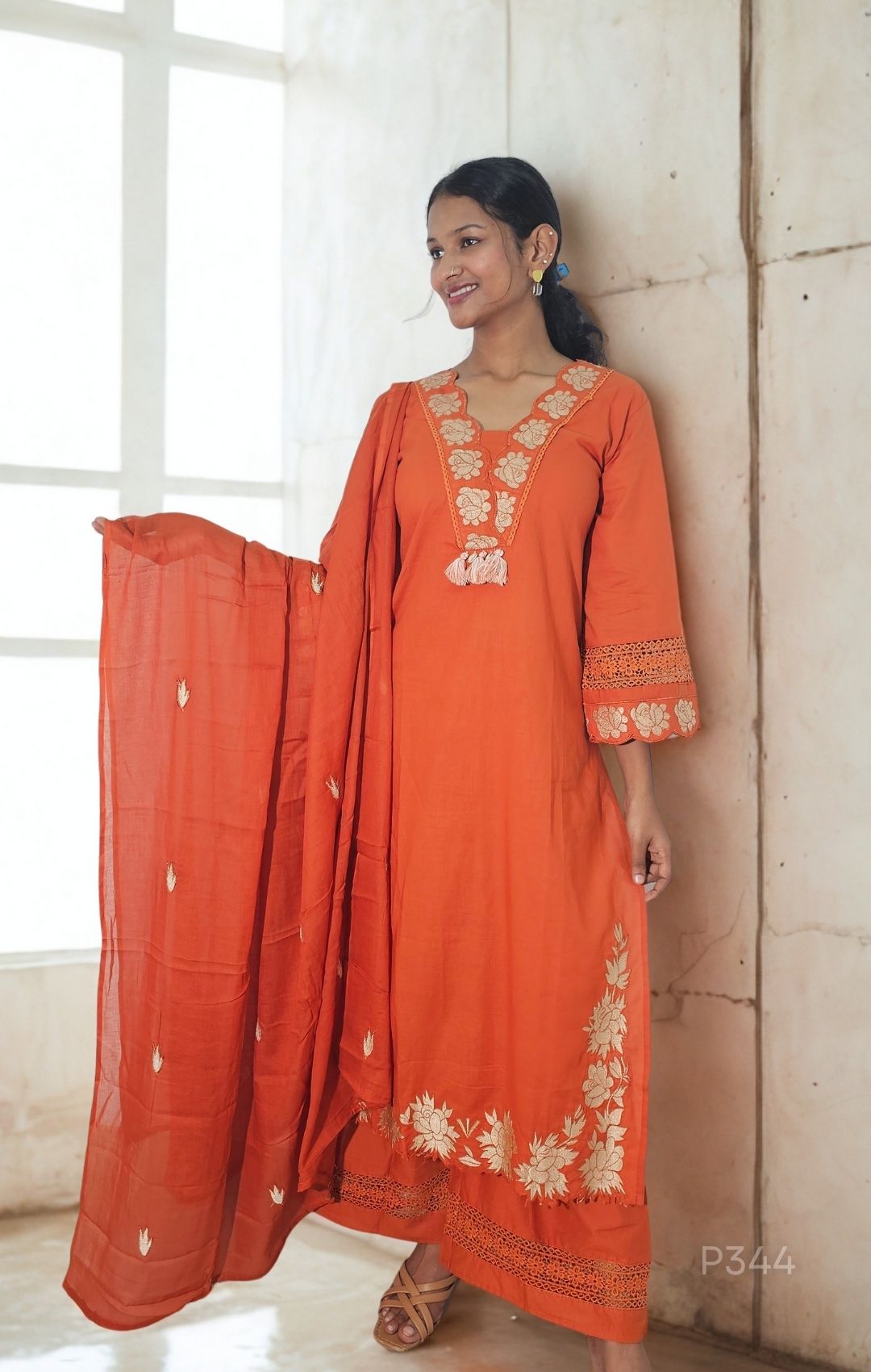 Woman wearing an orange embroidered traditional outfit with a plain background